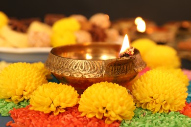 Photo of Diwali celebration. Diya lamp, colorful rangoli and chrysanthemum flowers on table, closeup