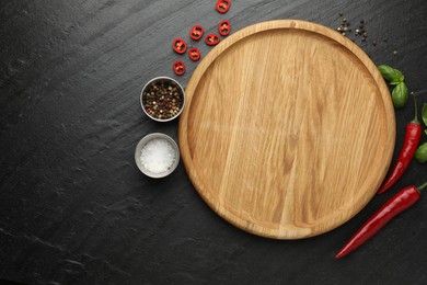 Photo of Cutting board, salt, spices, basil and chili peppers on black textured table, flat lay. Space for text
