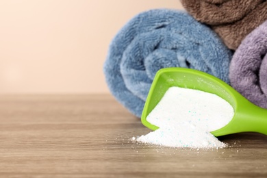 Photo of Scoop with washing powder and clean towels on table against color background, space for text. Laundry day