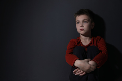 Photo of Sad little boy near black wall, space for text. Domestic violence concept