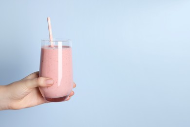 Photo of Woman holding glass of tasty smoothie on light blue background, closeup. Space for text
