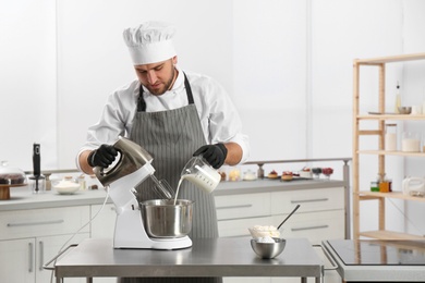 Photo of Male pastry chef preparing dough in mixer at kitchen table