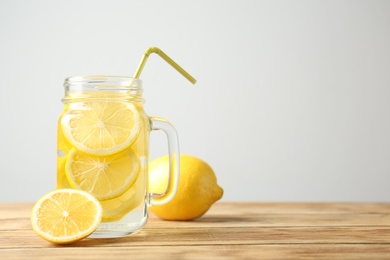Photo of Mason jar with lemon water and fresh fruit on wooden table
