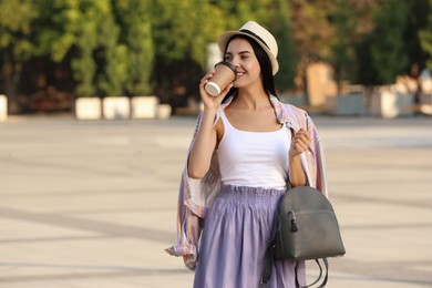 Photo of Beautiful young woman with stylish grey backpack drinking coffee on city street