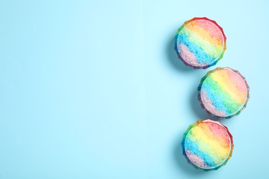 Photo of Rainbow shaving ice in glass dessert bowls on light blue background, flat lay. Space for text
