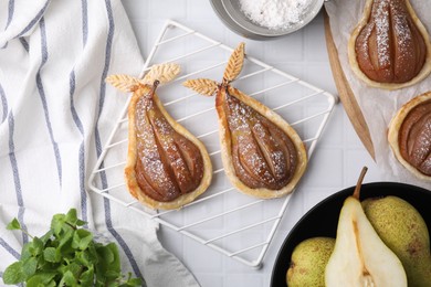Photo of Delicious pears baked in puff pastry with powdered sugar served on white tiled table, flat lay