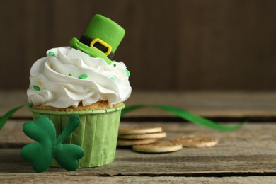 Photo of St. Patrick's day party. Tasty cupcake with green leprechaun hat topper on wooden table, closeup. Space for text