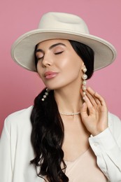 Young woman wearing elegant pearl jewelry on pink background