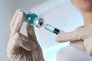 Photo of Doctor filling syringe with vaccine from vial on blurred background, closeup