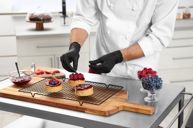 Photo of Male pastry chef preparing desserts at table in kitchen, closeup