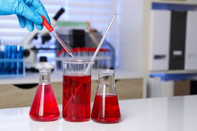 Photo of Laboratory analysis. Woman dripping red liquid into beaker on white table, closeup. Space for text