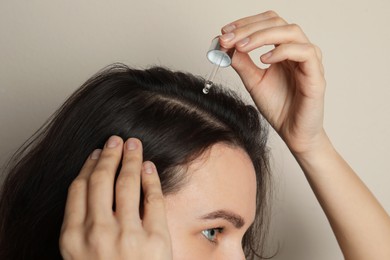 Photo of Woman applying oil onto hair on grey background, closeup. Baldness problem