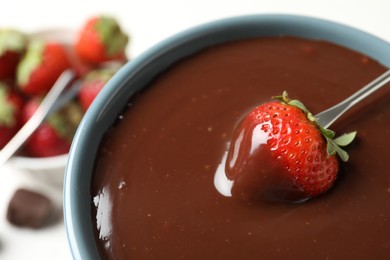 Photo of Dipping strawberry into fondue pot with chocolate, closeup