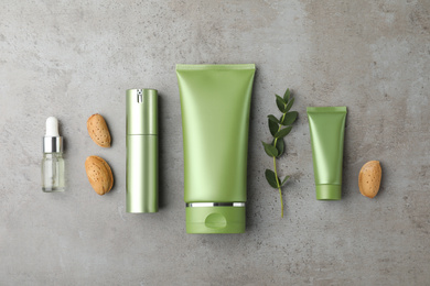 Photo of Set of cosmetic products, almond nuts and plant on grey table, flat lay