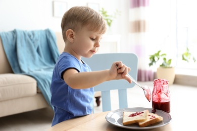 Photo of Little boy spreading jam on toasts at table in living room