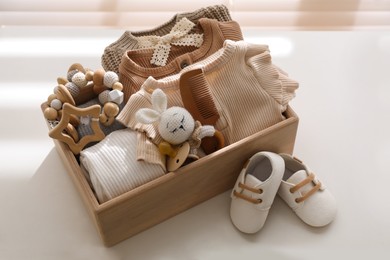 Photo of Wooden crate with children's clothes, toys and pacifier near shoes on white table in room