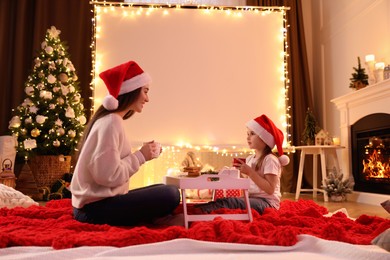 Photo of Mother and daughter near video projector screen at home. Cozy Christmas atmosphere