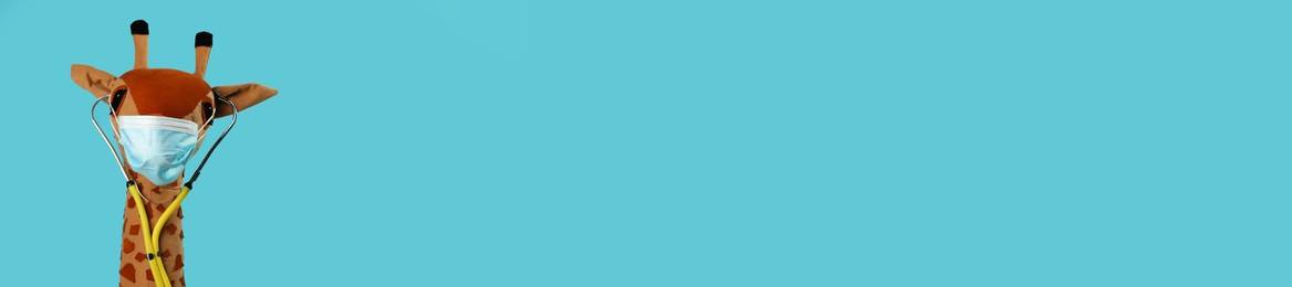 Photo of Toy giraffe with protective mask and stethoscope on light blue background, space for text. Pediatrician practice