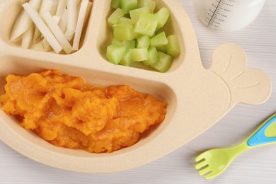 Photo of Healthy baby food. Section plate with delicious pumpkin puree and vegetables on white wooden table, closeup