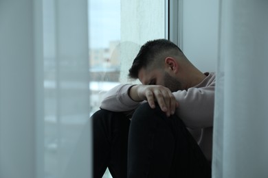 Photo of Sad man sitting near window at home