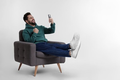 Photo of Happy young man using smartphone in armchair on white background, space for text