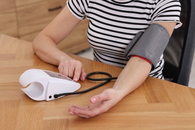 Photo of Woman measuring her blood pressure with tonometer at wooden table indoors, closeup