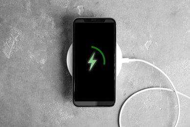 Photo of Mobile phone charging with wireless pad on grey stone table, top view
