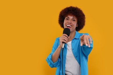 Photo of Curly young woman with microphone singing on yellow background, space for text