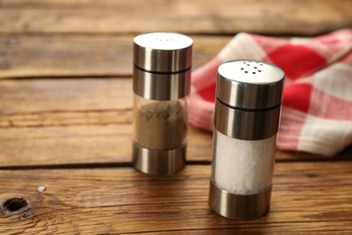 Photo of Salt and pepper shakers with napkin on wooden table, closeup