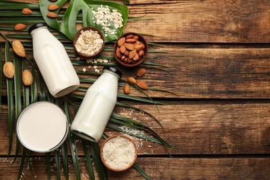 Photo of Different vegan milks and ingredients on wooden table, flat lay. Space for text