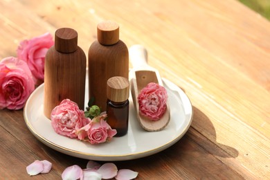 Photo of Bottles of rose essential oil and flowers on wooden table, space for text