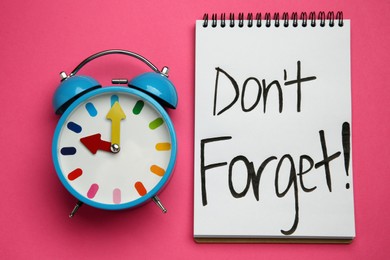 Photo of Alarm clock and notebook with text Don't forget on pink background, flat lay. Reminder concept