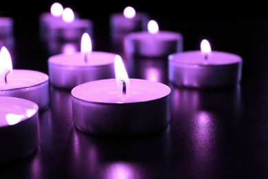 Image of Beautiful burning violet candles on black background, closeup. Funeral attributes