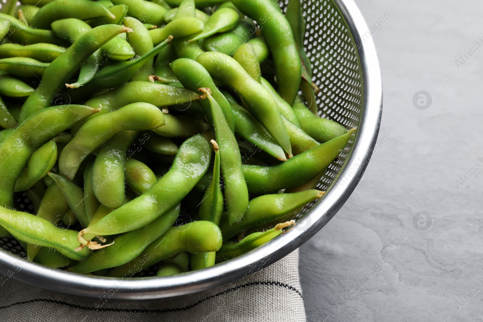 Photo of Sieve with green edamame beans in pods on table, closeup