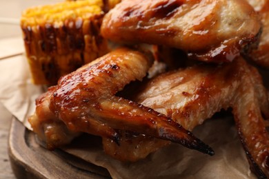 Photo of Delicious baked chicken wings and grilled corn served on wooden table, closeup