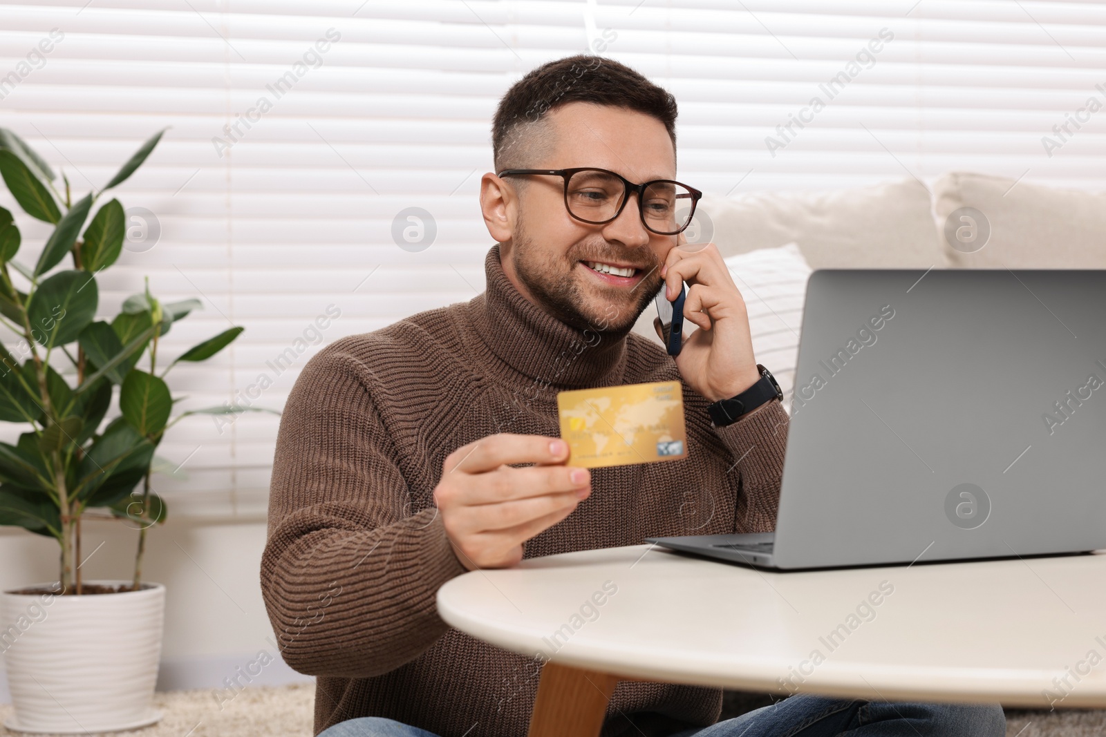 Photo of Handsome man with credit card using smartphone and laptop for online shopping at home