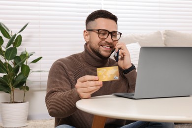 Handsome man with credit card using smartphone and laptop for online shopping at home