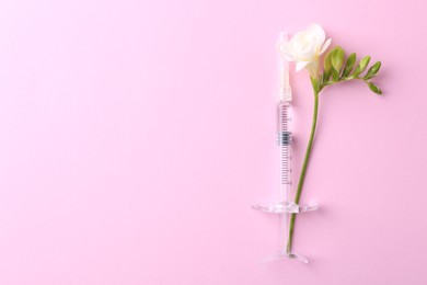 Photo of Cosmetology. Medical syringe and freesia flower on pink background, top view. Space for text