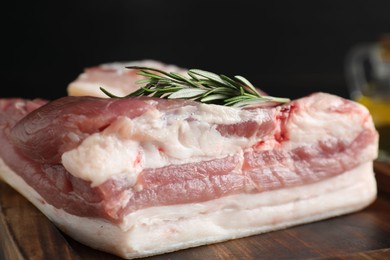 Piece of raw pork belly, salt and rosemary on wooden board, closeup