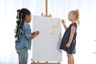 Photo of Cute little children drawing on easel at painting lesson indoors