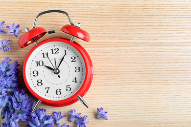 Photo of Red alarm clock, spring flowers and space for text on wooden table, flat lay. Time change