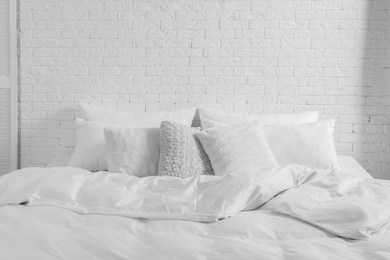 Photo of Large comfortable bed with pillows and blanket near white brick wall indoors. Stylish interior