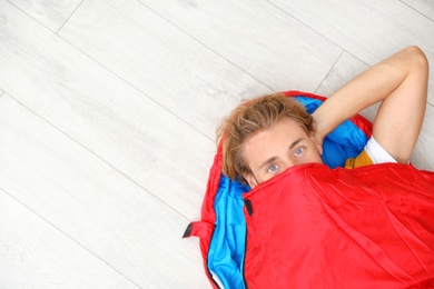 Photo of Young man in comfortable sleeping bag on floor, top view. Space for text