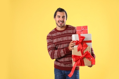 Photo of Happy man in Christmas sweater and hat holding gift boxes on yellow background