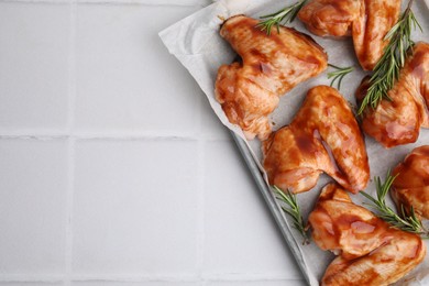 Photo of Raw marinated chicken wings and rosemary on light tiled table, top view. Space for text