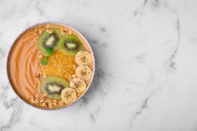 Photo of Bowl of delicious fruit smoothie with fresh banana, kiwi slices and granola on white marble table, top view. Space for text