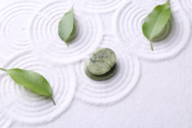Photo of Zen garden stones and green leaves on white sand with pattern, flat lay