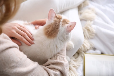 Photo of Woman with cute fluffy cat and book on bed, closeup