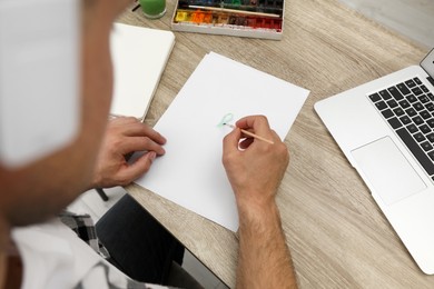 Photo of Man drawing with paints at table, above view. Distance learning