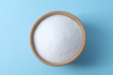 Photo of Organic white salt in bowl on light blue background, top view